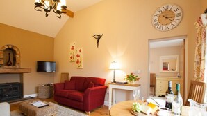 A cozy living room with a fireplace, red sofa, wooden dining table with food, and a large wall clock. - 1 Bed in Howden (oc-g0181) (Saltmarshe)