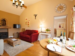A cozy living room with a fireplace, red sofa, wooden dining table with food, and a large wall clock. - 1 Bed in Howden (oc-g0181) (Saltmarshe)