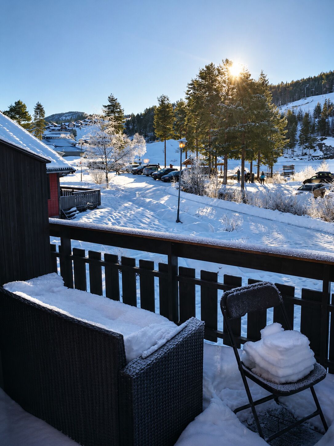 Een sneeuwbedekt terras met een stoel en een bank, uitkijkend op een besneeerd landschap met gebouwen en bomen.