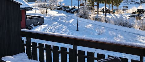 Een sneeuwbedekt terras met een stoel en een bank, uitkijkend op een besneeerd landschap met gebouwen en bomen.