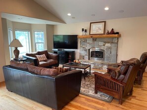 A living room with a stone fireplace, leather sofas, a flat-screen TV, and a wooden coffee table. - Large home in the Tahoe Keys! (South Lake Tahoe)