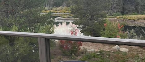 En balkong med ett runt bord och stolar, med utsikt över ett skogsområde och en sjö.