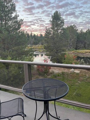 A balcony with a round table and chairs, overlooking a forested area with a lake. - Large home in the Tahoe Keys! (South Lake Tahoe)