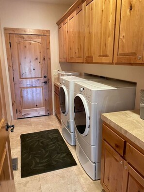 A laundry room with two front-loading washing machines, wooden cabinets, a door, and a black rug. - Large home in the Tahoe Keys! (South Lake Tahoe)