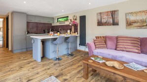 Una cocina moderna con una isla central, taburetes de bar, un sofá con cojines a rayas y una mesa de centro de madera.