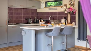 Una cocina moderna con una isla central, taburetes de bar, un televisor y un reloj en la pared.
