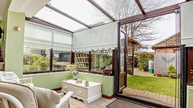 Ein Wintergarten mit Glastür zu einem Garten, ein weißes Sofa und ein kleiner Tisch mit einer Vase.