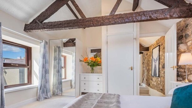 Een slaapkamer met een groot bed, een stenen muur, een spiegel en een raam.