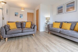 Ein Wohnzimmer mit zwei grauen Sofas, Holzdielen und einer weißen Wand mit gerahmten Bildern.