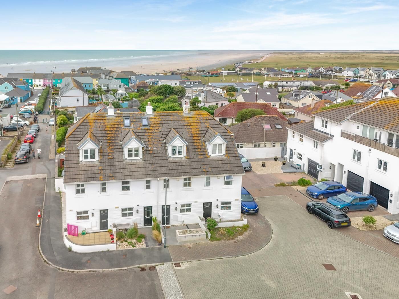 A residential area with houses, a beach in the background, and parked cars.