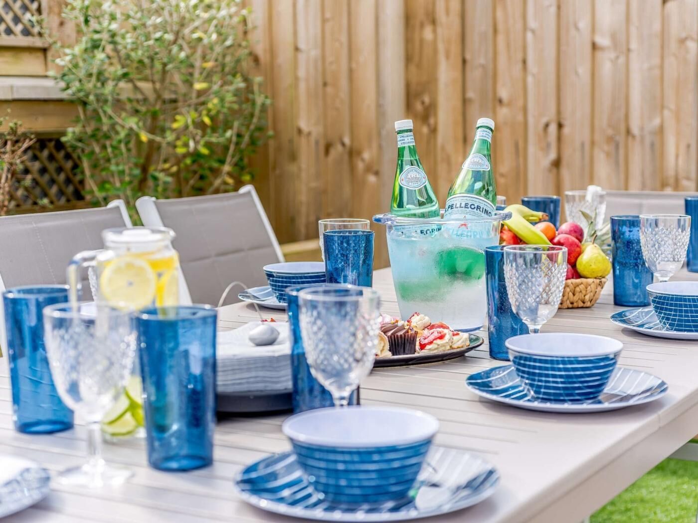 Une table dressée avec de la vaisselle en verre bleue, un pichet et un panier de fruits.