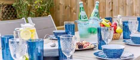 Ein Tisch, gedeckt mit blauem Glas, einer Karaffe und einem Obstkorb.