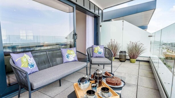 A balcony with a sofa, chairs, and a tray with teapots and a cake. - 5 Bed in Bideford (oc-80650) (Westward Ho!)