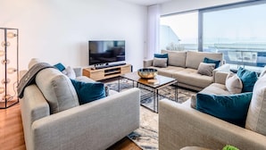 A modern living room with a flat-screen TV, two sofas, a coffee table, and a large window offering a view. - 5 Bed in Bideford (oc-80650) (Westward Ho!)