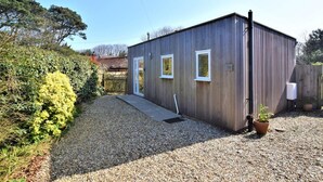 A small, single-story wooden building with a gravel driveway, a wooden fence, and a potted plant.