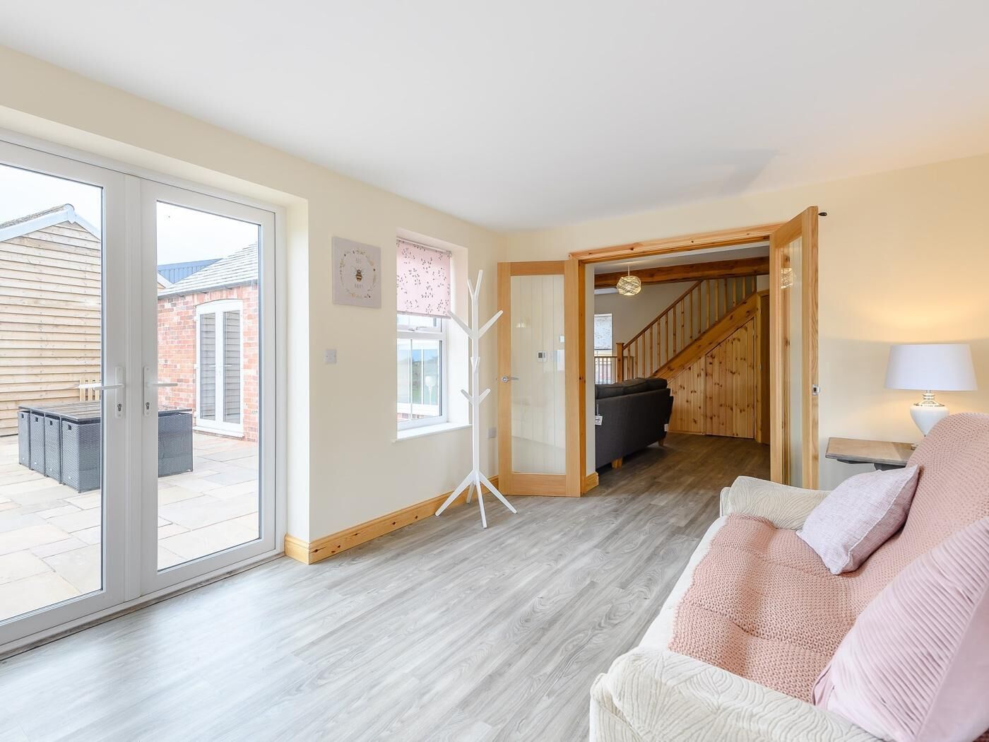 A spacious living area with a large sliding glass door leading to an outdoor patio, a wooden staircase, and a cozy seating area with a sofa and a lamp.