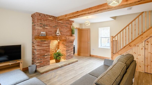 Ein Wohnzimmer mit Kamin aus Ziegelsteinen, einem Fernseher, einer Couch und einer Treppe.
