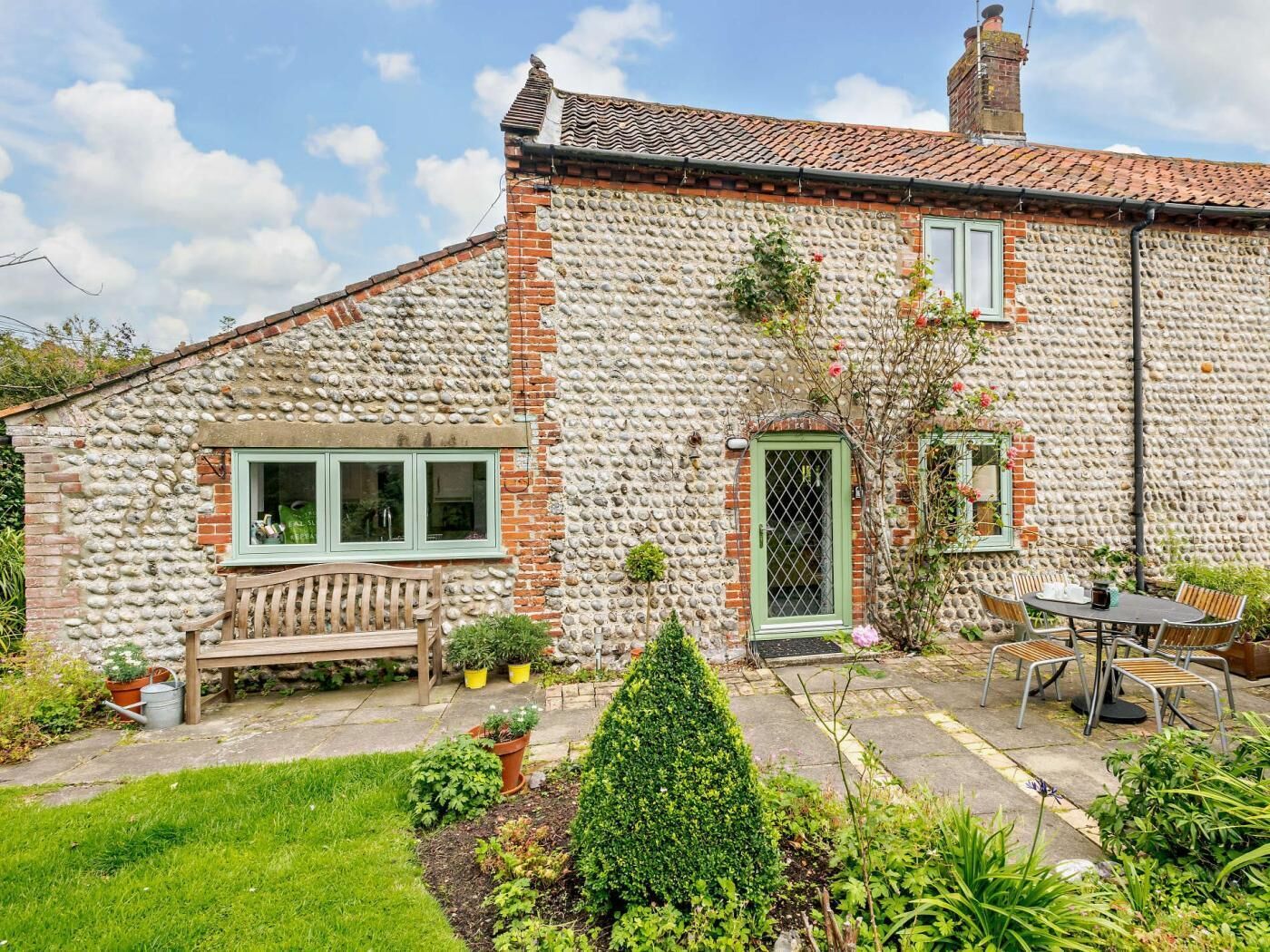 A stone house with a green door, a bench, and a patio with chairs and a table.
