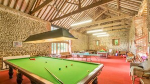 Una sala de billar con mesa de pool, varias mesas más pequeñas y una pared de piedra.