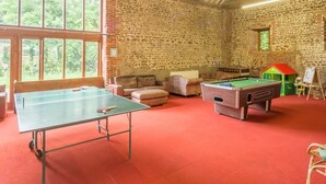 Una habitación con mesa de ping pong, mesa de billar y una pared de piedra.