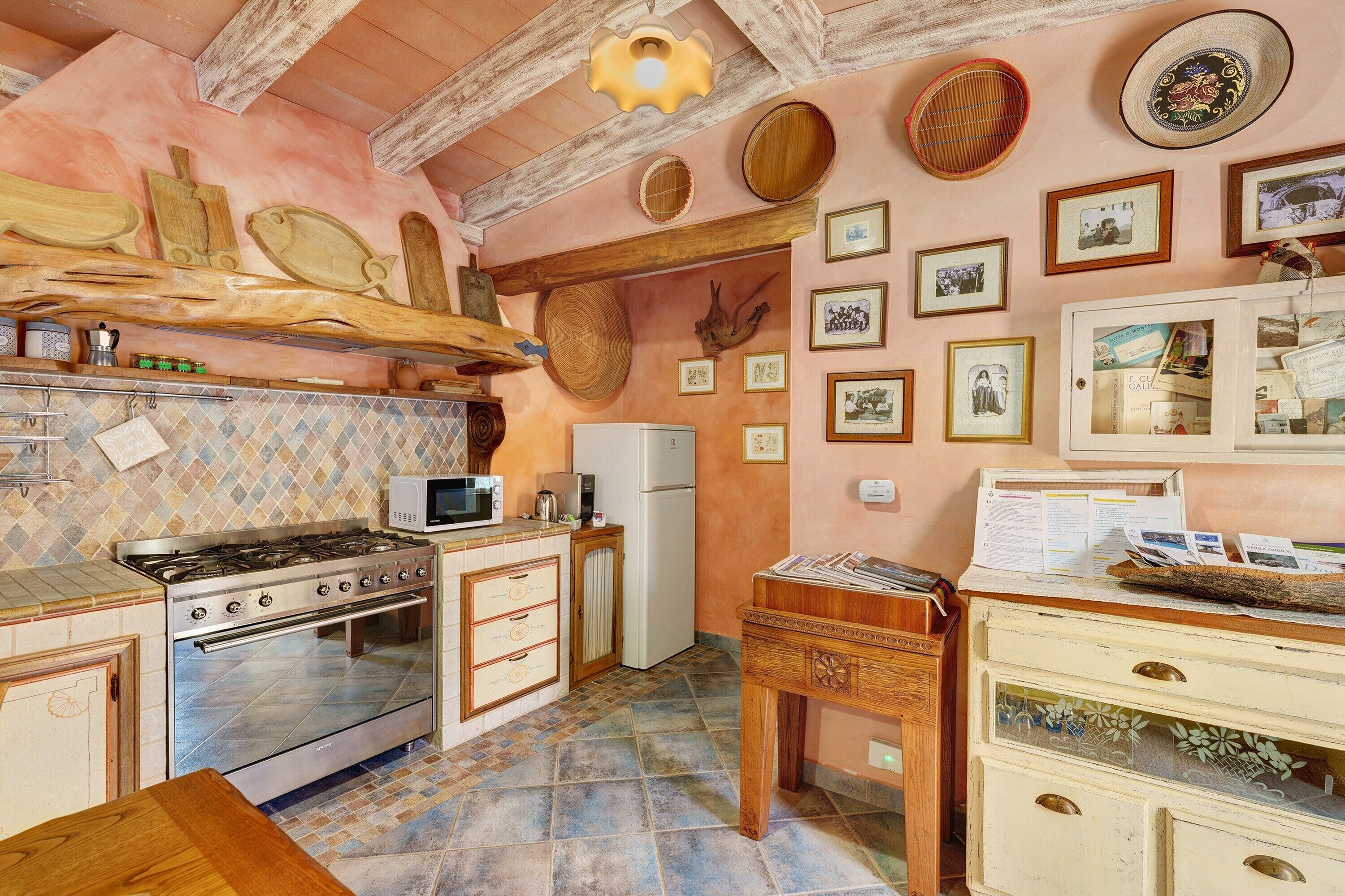 A kitchen with a gas stove, oven, microwave, refrigerator, and a wooden cabinet with drawers.