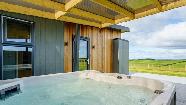 Un jacuzzi con terraza de madera y vistas a un paisaje verde.