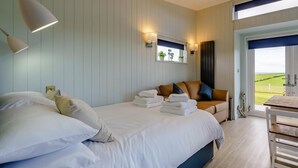 Un dormitorio con cama, lámparas de noche, sofá, mesa y vistas al exterior.