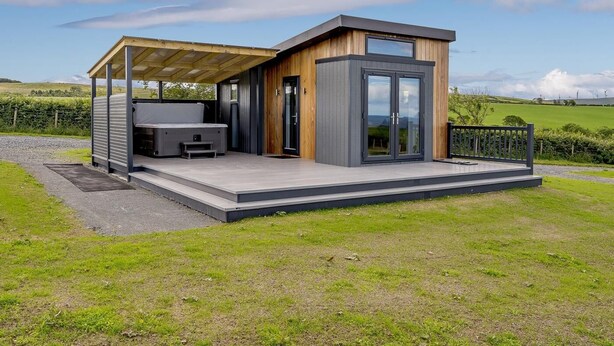 Una estructura moderna al aire libre con un espacio de estar techado, un jacuzzi y una sala acristalada.