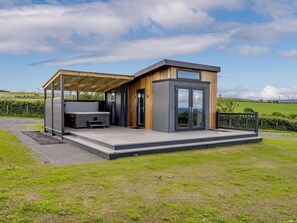 Una estructura moderna al aire libre con un espacio de estar techado, un jacuzzi y una sala acristalada.