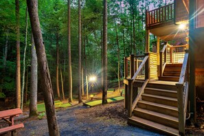 A wooden cabin with a staircase leading to a deck, surrounded by a forest. - Cedar Cabin Stay (Sevierville)