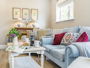 A cozy living room with a light blue sofa, a coffee maker, a white table, and a window with blinds. - 2 Bed in York (oc-84001) (Crayke)