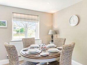 A dining area with a round table, wicker chairs, a clock, and a window with blinds. - 2 Bed in York (oc-84001) (Crayke)