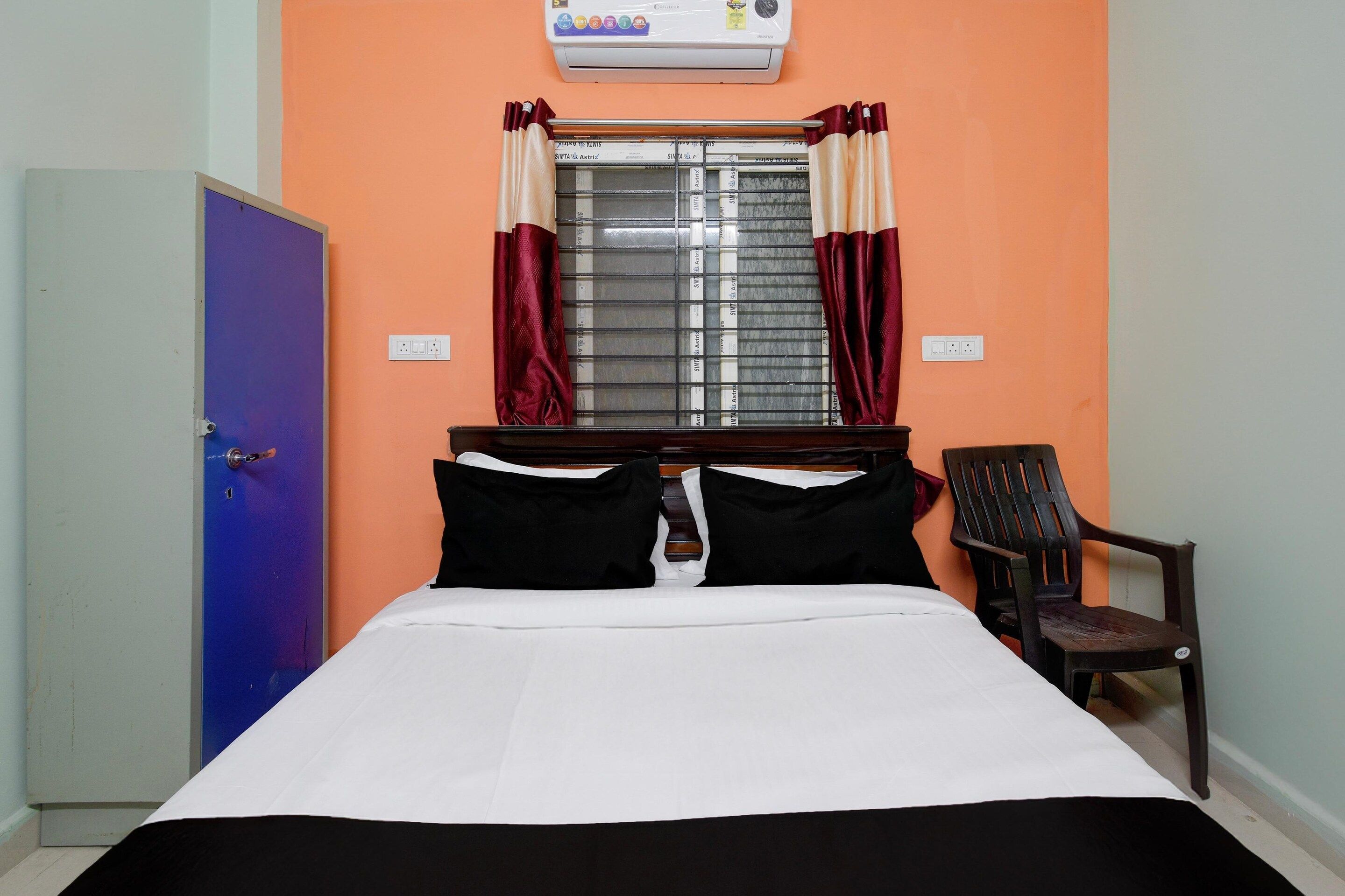 A bedroom with a bed, a window with curtains, a chair, and an air conditioner.