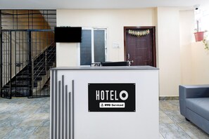 A reception desk with a 'HOTEL' sign and a 'YOYO-Serviced' label, a staircase, a door with a decorative wreath, and a grey sofa. - Classic Hotel O SLN Gachibowli (Hyderabad)