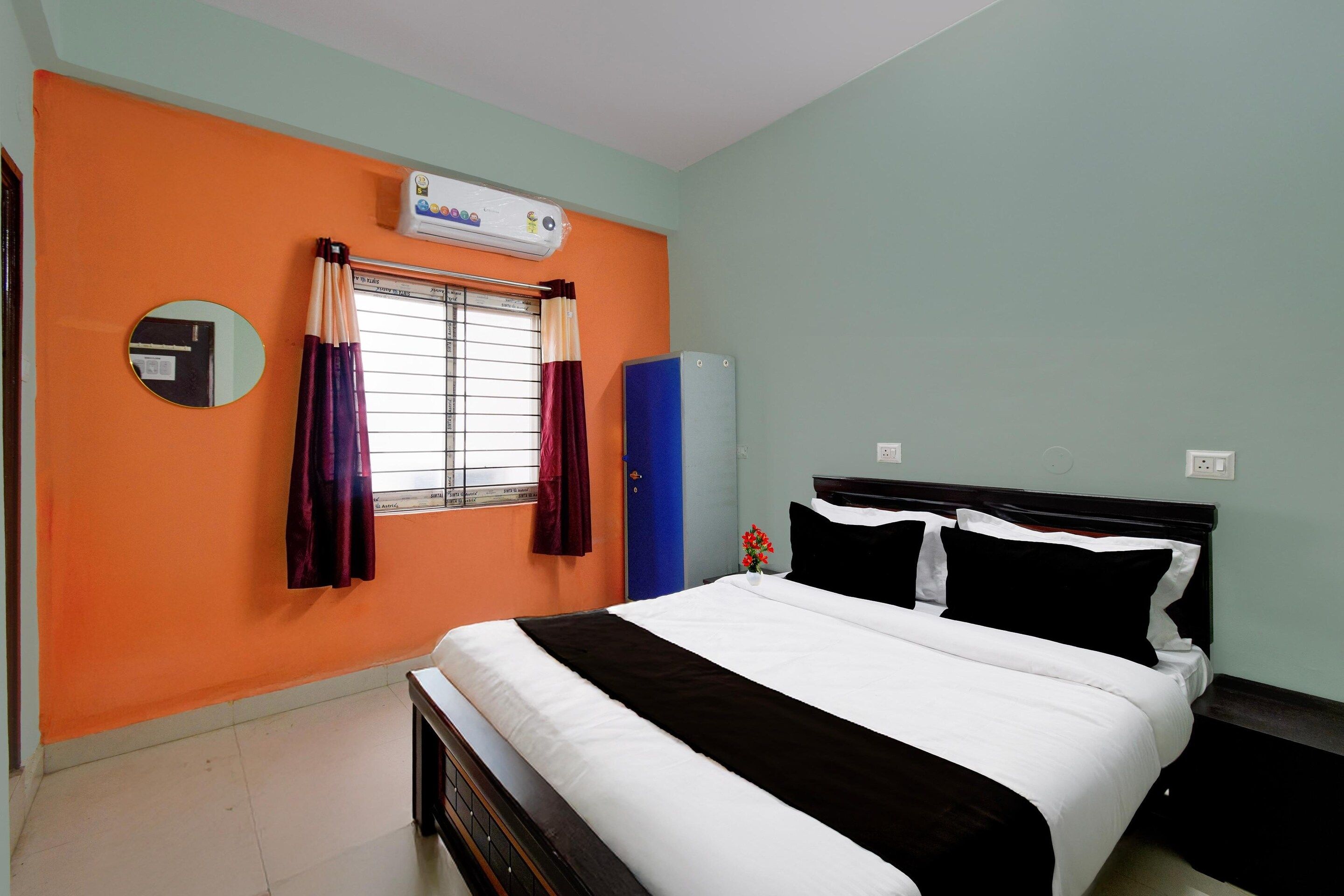 A hotel room with a bed, a wardrobe, a mirror, and a window with curtains.
