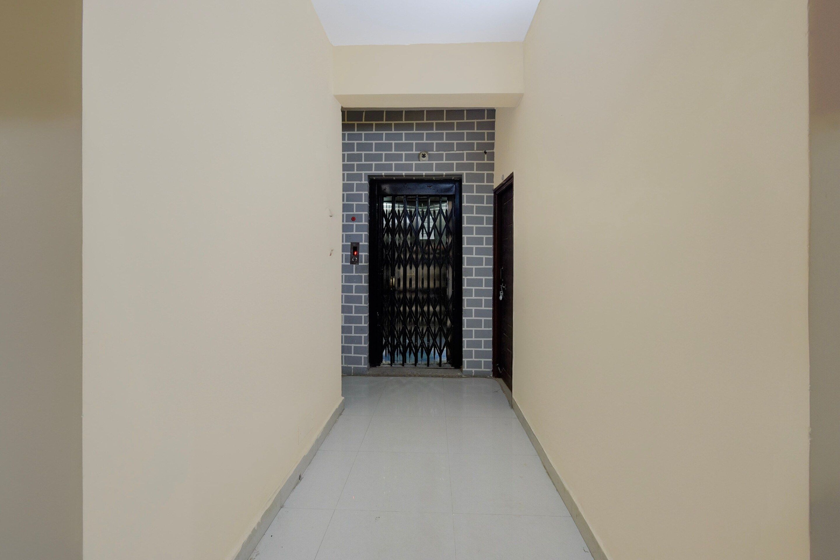 A corridor with a door at the end, a tiled floor, and a wall with a brick pattern.