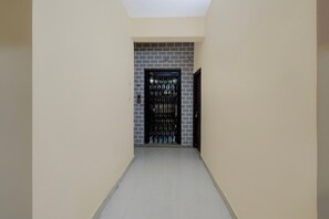 A corridor with a door at the end, a tiled floor, and a wall with a brick pattern. - Classic Hotel O SLN Gachibowli (Hyderabad)