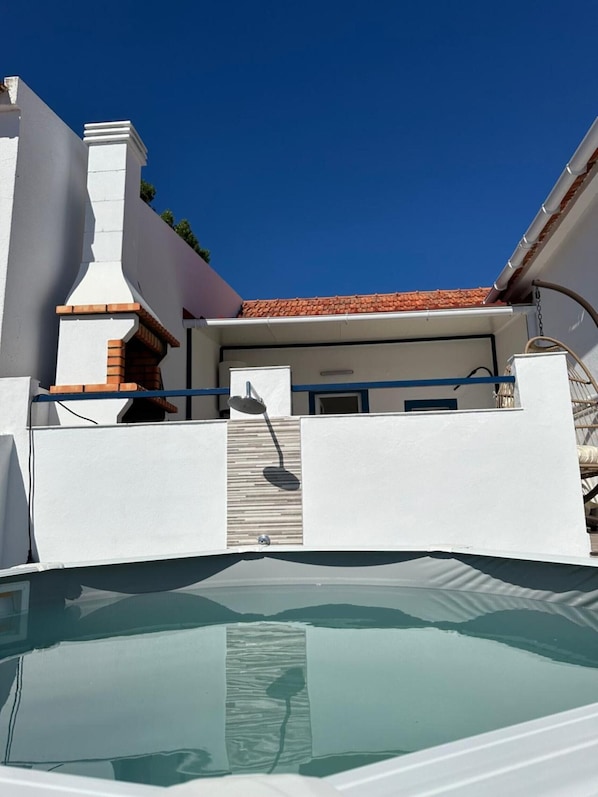 Une piscine à l’extérieur blanc, dotée d’une cheminée et d’un toit recouvert de tuiles.
