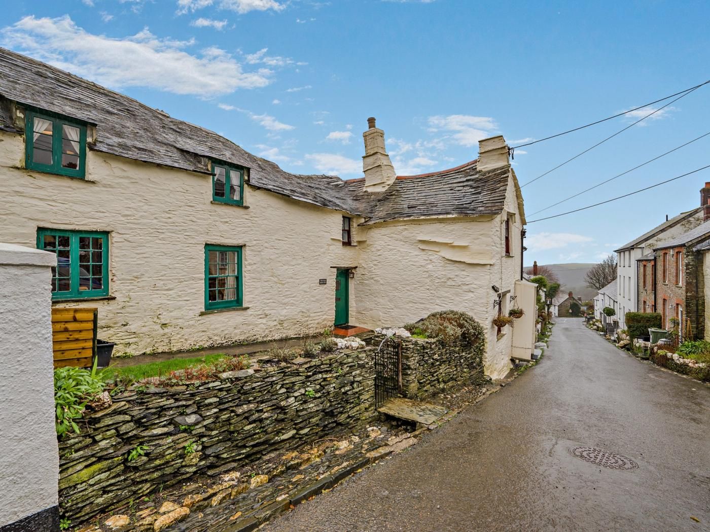 A narrow street lined with traditional white buildings with green window frames and stone walls.