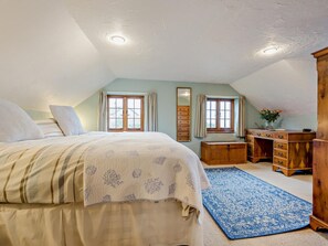 Ein Schlafzimmer mit einem Bett, einem Schreibtisch, einer Kommode und zwei Fenstern.