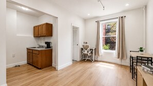 Una cocina moderna con armarios de madera, un comedor con mesa y sillas, y un ventanal con vista a un edificio.