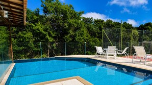 A swimming pool with tiled edges, surrounded by a fence and trees, with white lounge chairs. - Villa Serena | Vacation Home for Families and Groups (Armação dos Búzios)