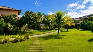 A well-maintained garden with a paved pathway, palm trees, and a building with a tiled roof. - Villa Serena | Vacation Home for Families and Groups (Armação dos Búzios)