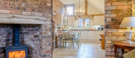 A cozy living room with a fireplace, a dining area, and a kitchen visible through an archway.