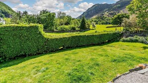 Üppiges Grün mit einer Steinmauer, einer Wiese und einem Berg im Hintergrund.