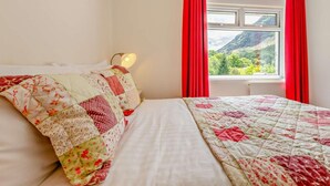 Ein Schlafzimmer mit einem Bett, einem Nachttisch, einer Lampe und einem Fenster mit Vorhängen.