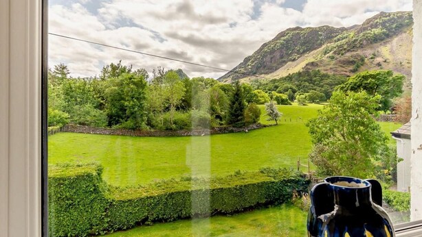 Ein Blick auf eine üppige grüne Landschaft mit einem Berg im Hintergrund, einem klaren Himmel und einem Einblick in einen Fensterrahmen.