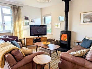 A cozy living room with a fireplace, leather sofas, a TV, and a dining table. - 2 Bed in Cockermouth (oc-sz381) (Wythop)