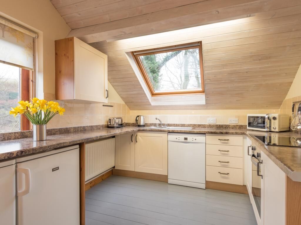 Een moderne keuken met dakraam, witte kasten en een klein raam.