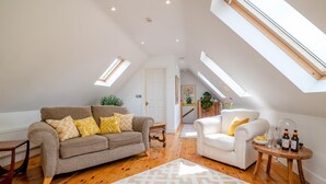 Un salón estilo loft con sofá marrón, sillón blanco, suelo de madera y tragaluces.